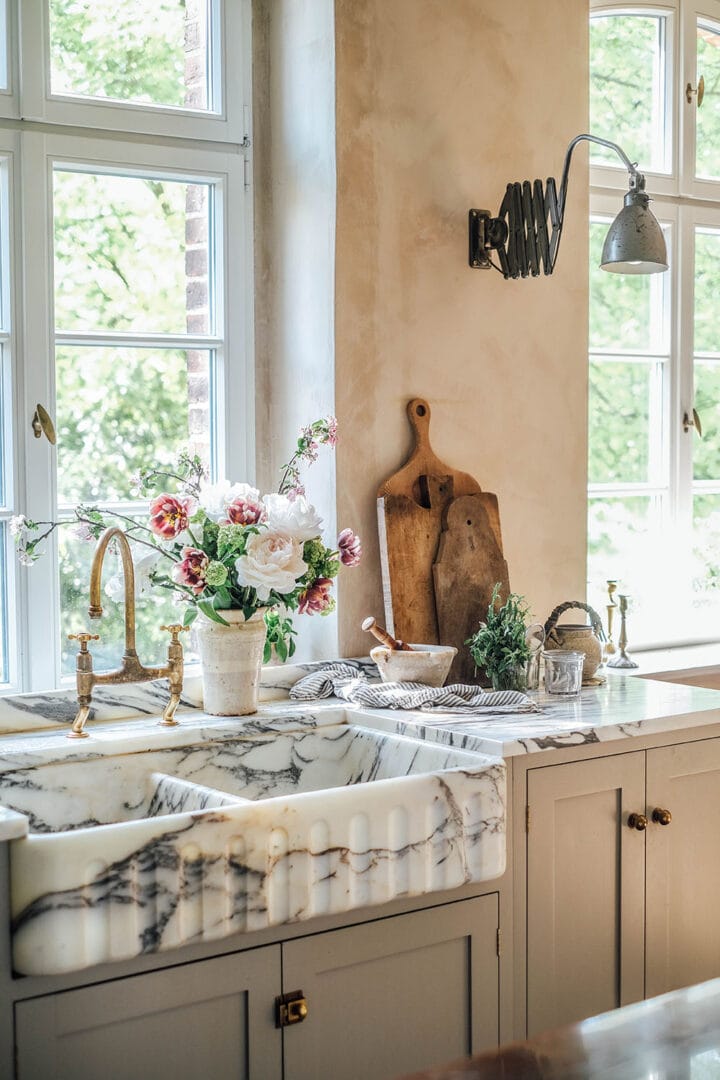 kitchen without upper cabinets, marble countertop and sink, gold fixture aand large windows